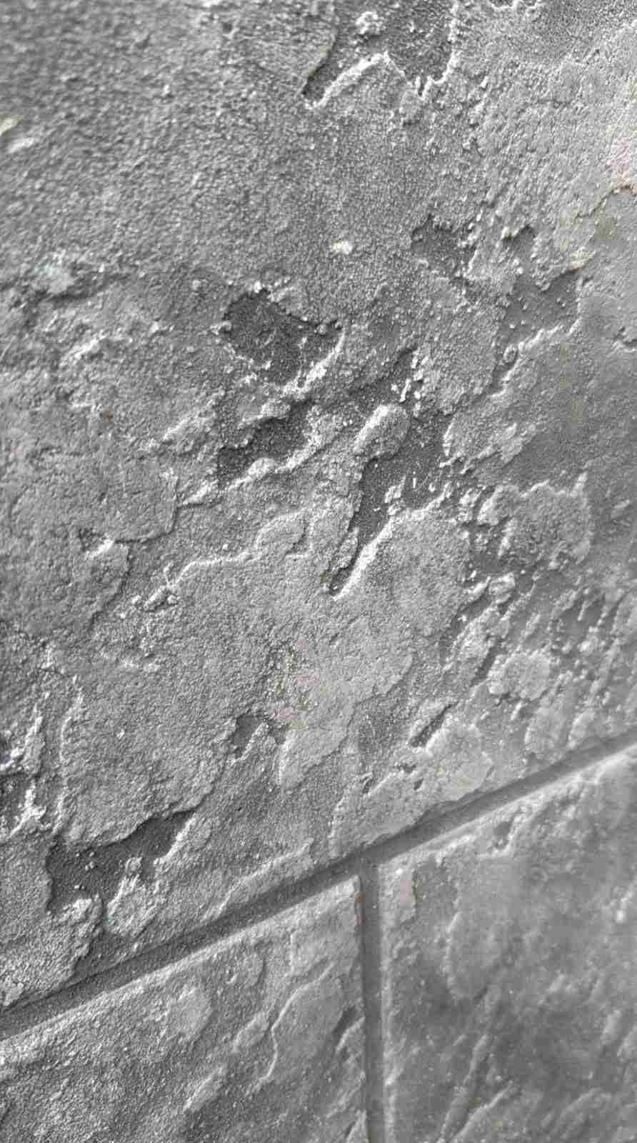 Primer plano de un muro de piedra gris rugosa con un borde de azulejos en la parte inferior.