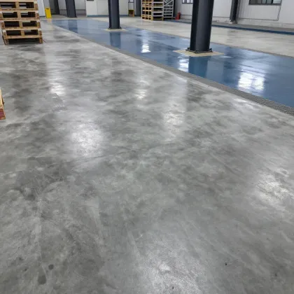 Trabajador pintando una junta blanca del suelo con un rodillo largo en un espacio industrial interior.