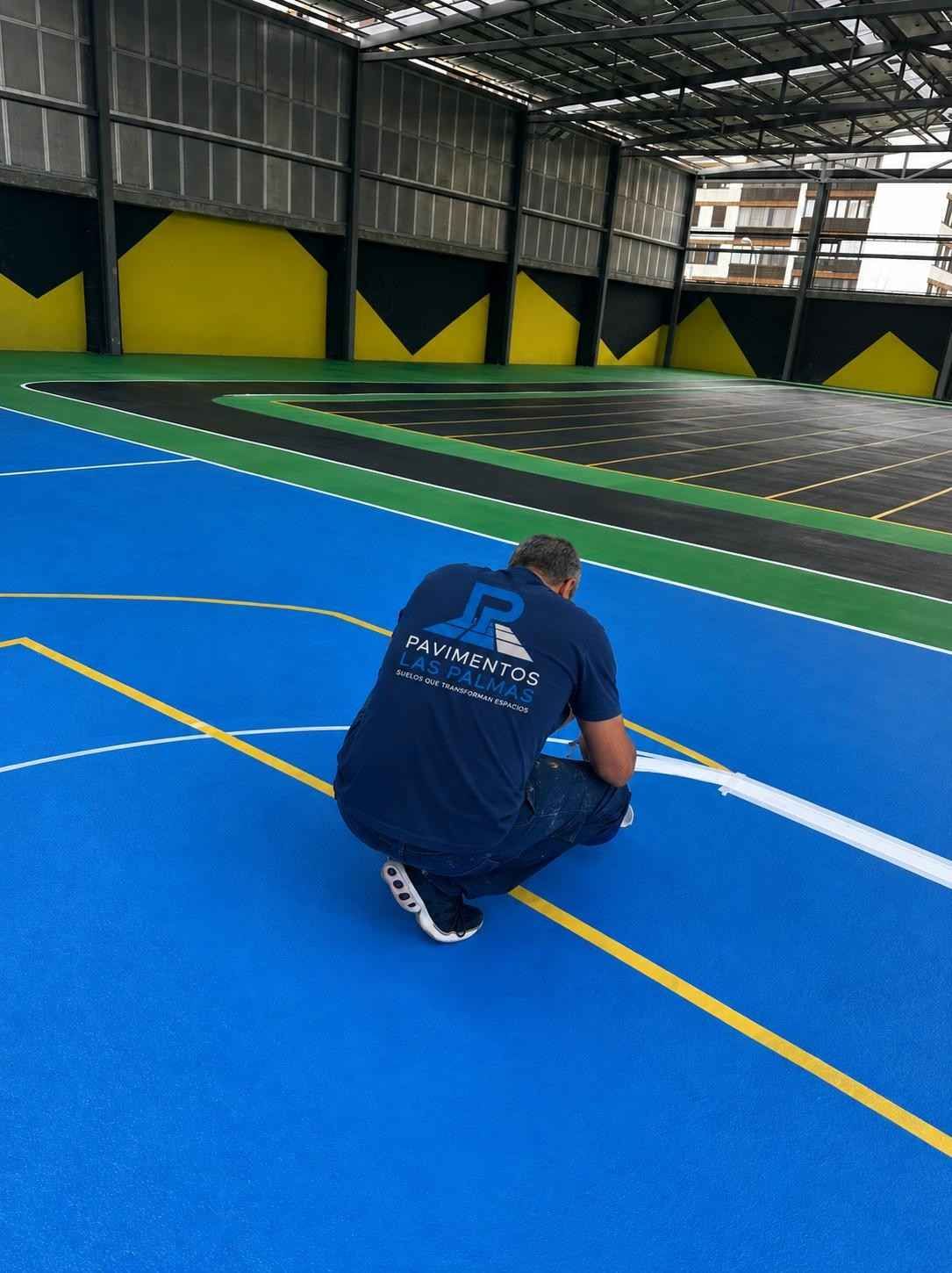 Persona agachada en una cancha deportiva cubierta azul con líneas amarillas en un gimnasio.