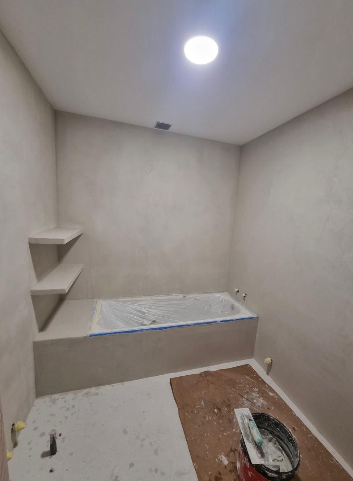 Habitación pequeña sin terminar con un banco empotrado, estantes en la pared y una luz brillante en el techo.