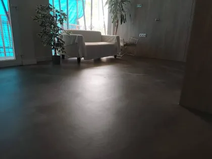 Trabajador pintando una junta blanca del suelo con un rodillo largo en un espacio industrial interior.