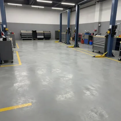 Trabajador pintando una junta blanca del suelo con un rodillo largo en un espacio industrial interior.