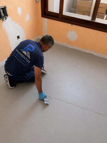 Trabajador pintando una junta blanca del suelo con un rodillo largo en un espacio industrial interior.