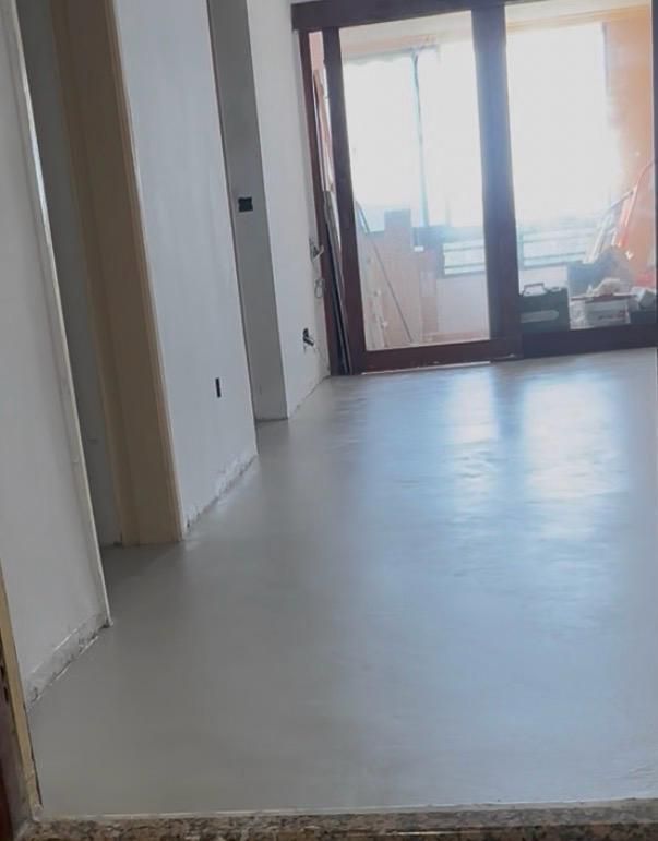Habitación vacía sin amueblar, con paredes blancas y suelo gris claro, que da a una puerta de cristal o a un balcón.