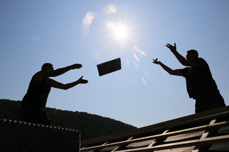 2 couvreurs en contre-jour s'envoient des tuiles sur un toit
