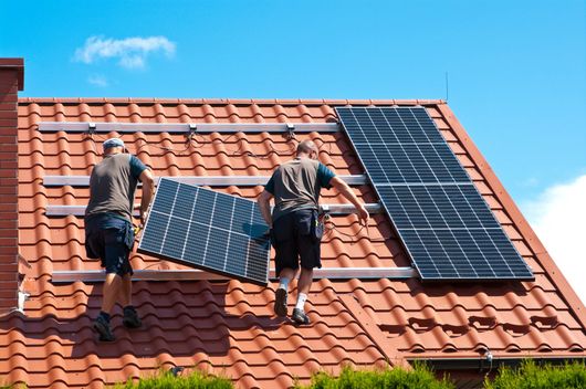 2 couvreurs montent un panneau solaire sur un toit