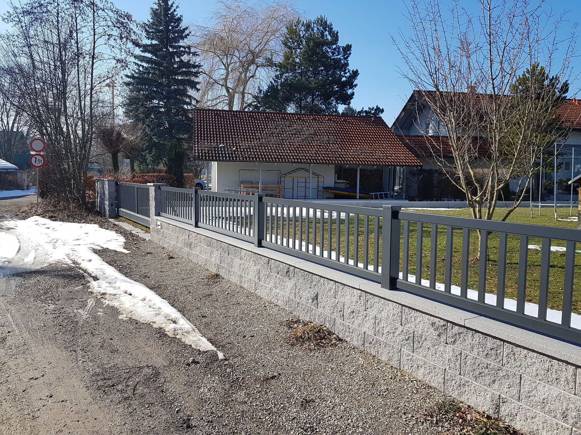 Ein Zaun mit einem Haus im Hintergrund und Schnee auf dem Boden.