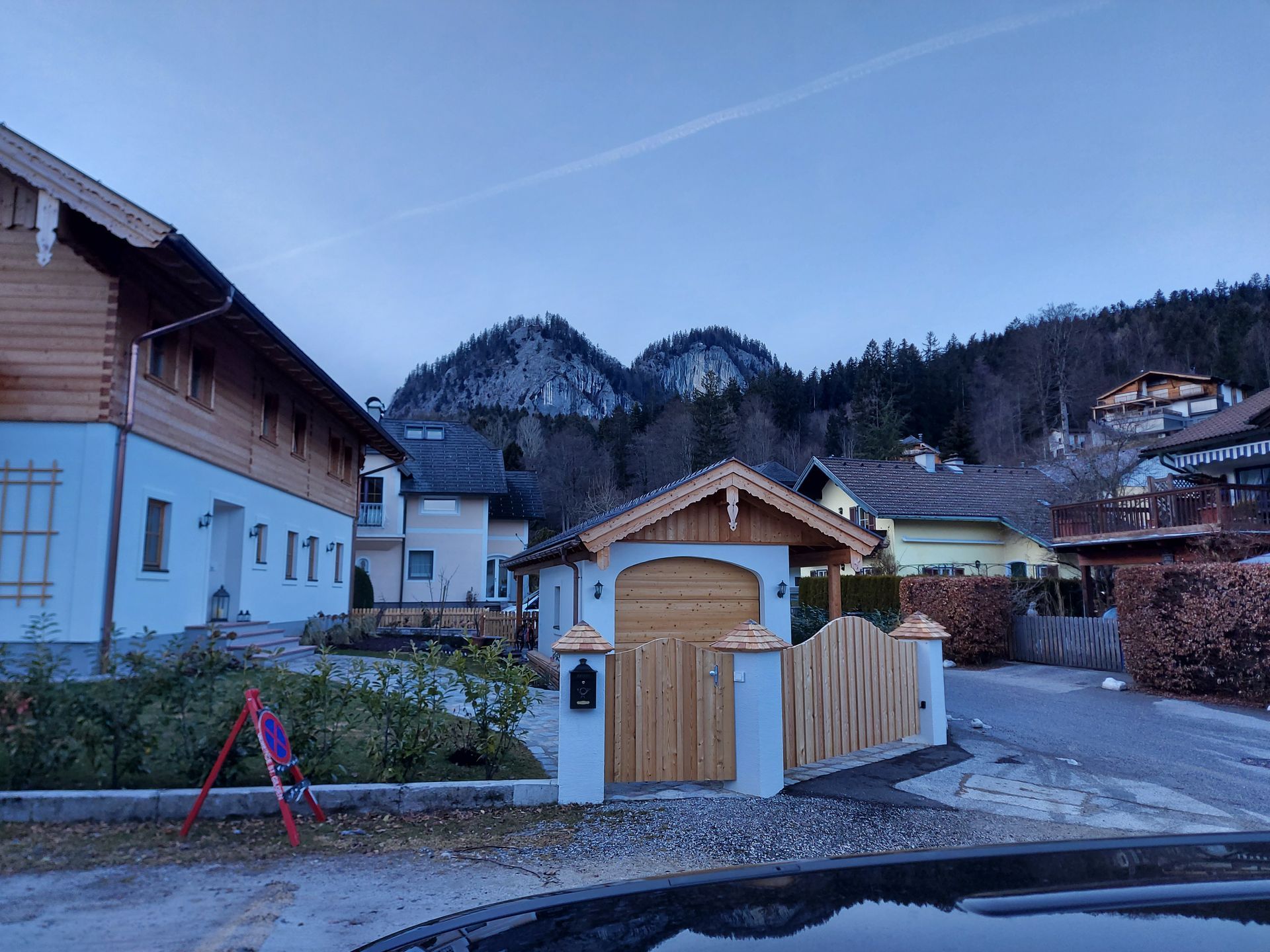 Vor einem Haus ist ein Auto geparkt, im Hintergrund sind Berge zu sehen.
