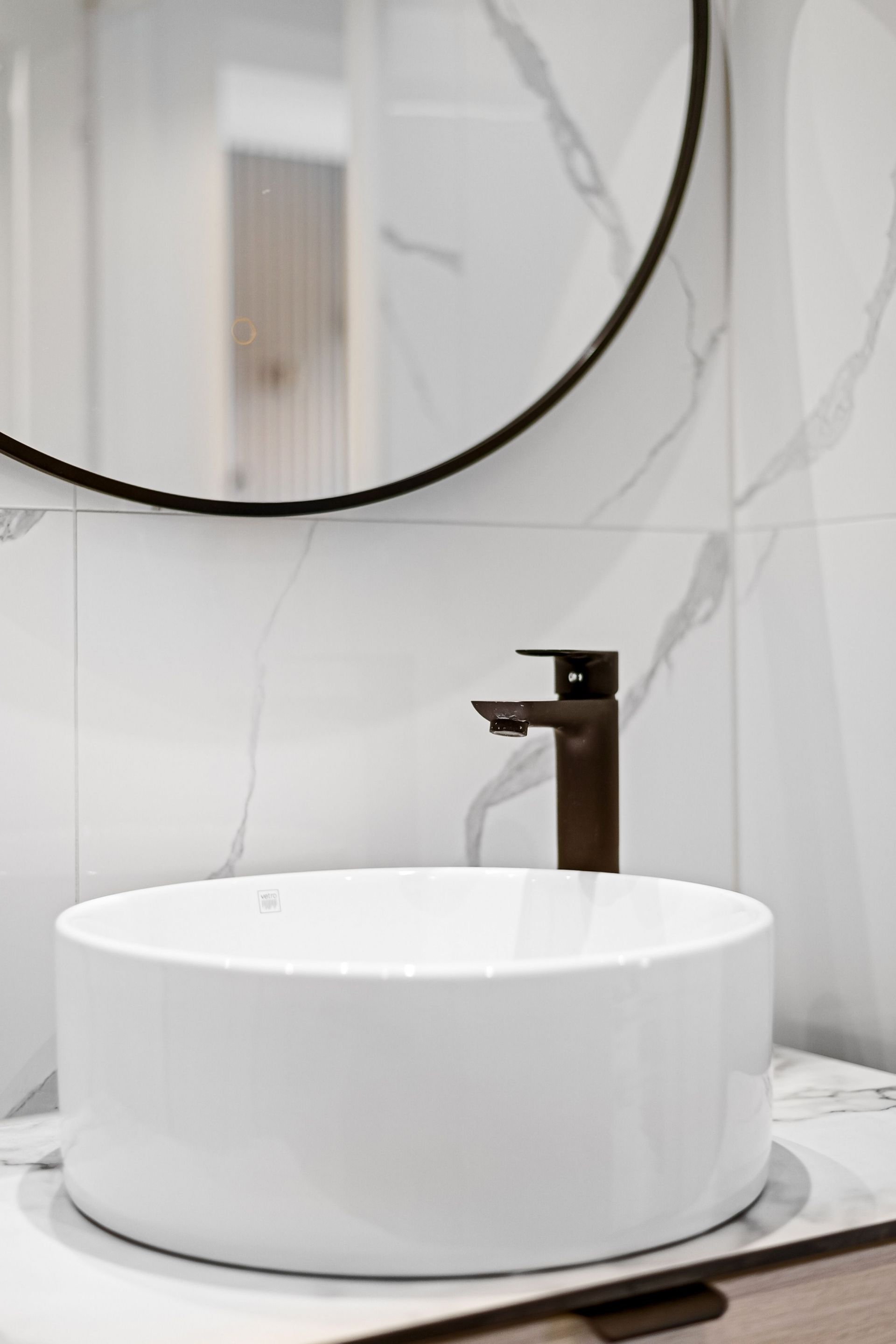 Lavabo moderne avec miroir rond, robinet marron et carrelage blanc effet marbre