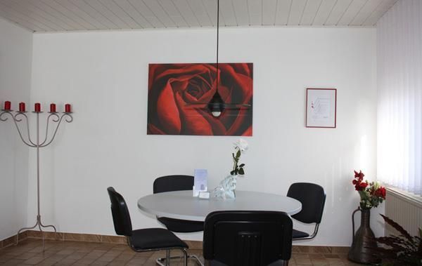 Ein Zimmer mit einem Tisch und Stühlen und einem Gemälde einer Rose an der Wand