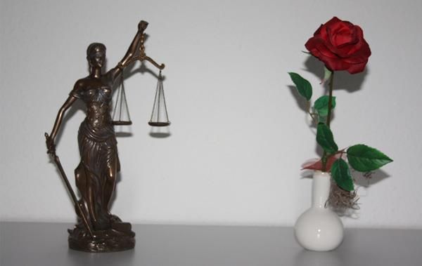 Eine Statue der Justitia neben einer Vase mit einer roten Rose