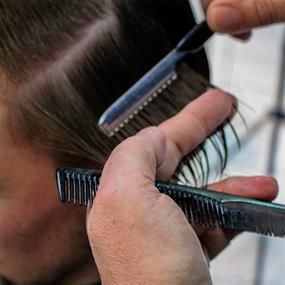 Ein Mann lässt sich von einem Friseur mit Kamm und Schere die Haare schneiden.