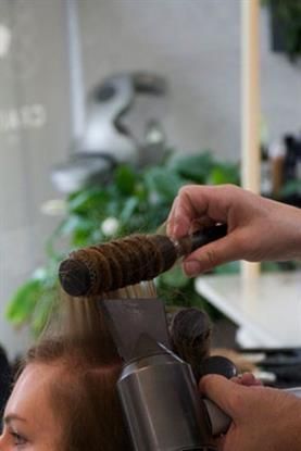 Eine Frau lässt sich von einem Friseur die Haare föhnen.