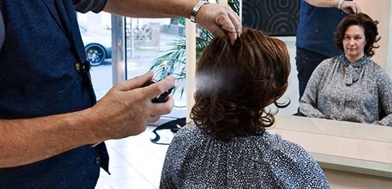 Ein Mann sprüht einer Frau in einem Salon die Haare.