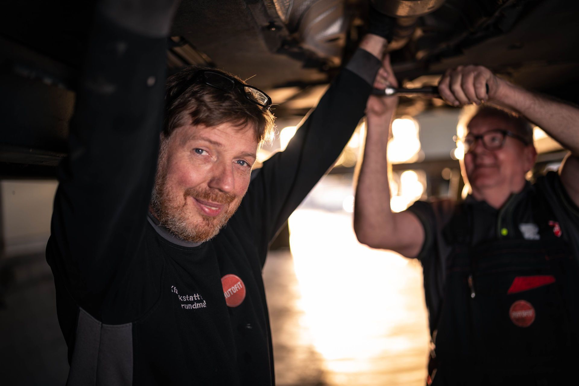Zwei Männer arbeiten in einer Garage an einem Auto.