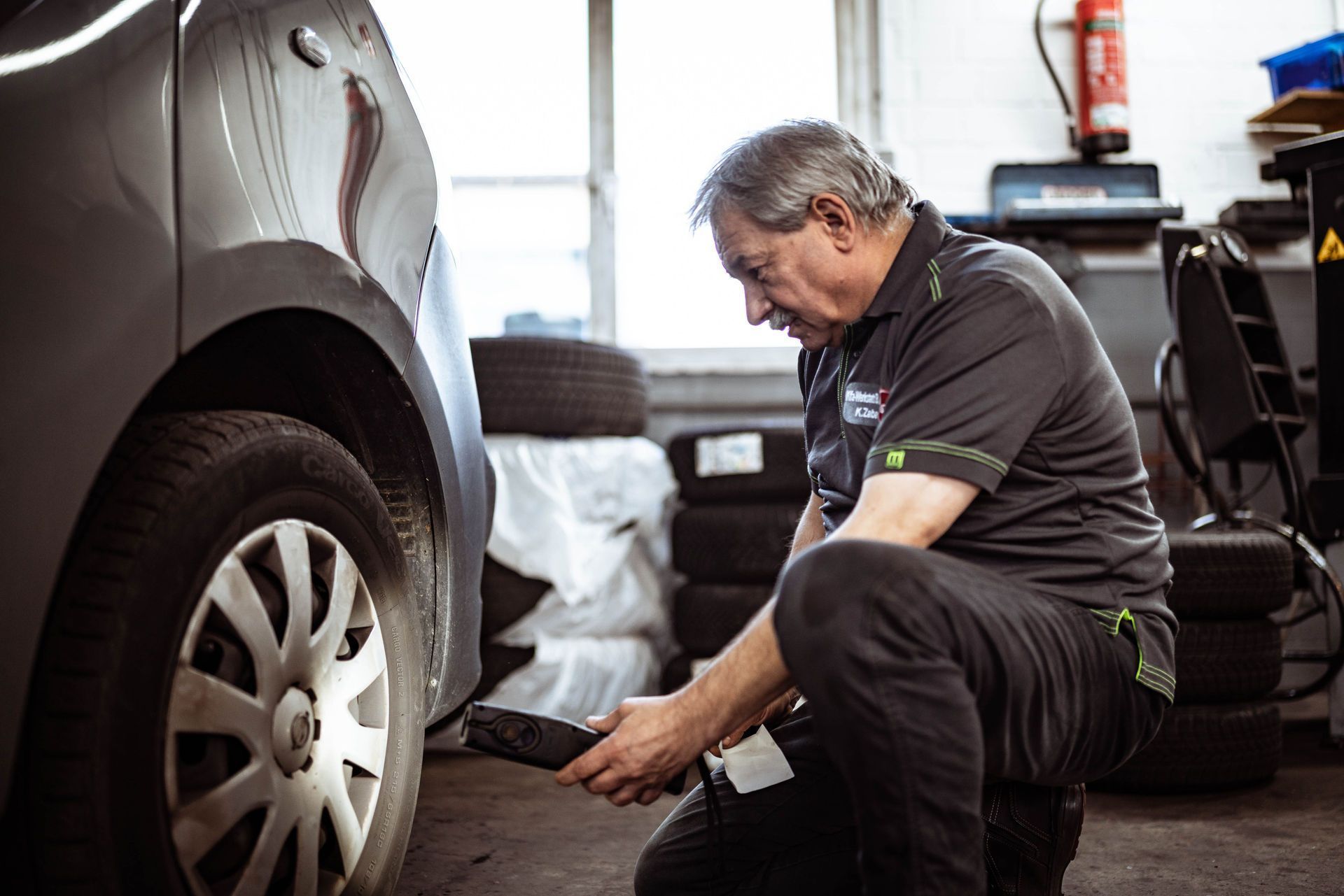 Ein Mann kniet vor einem Auto und betrachtet einen Reifen.
