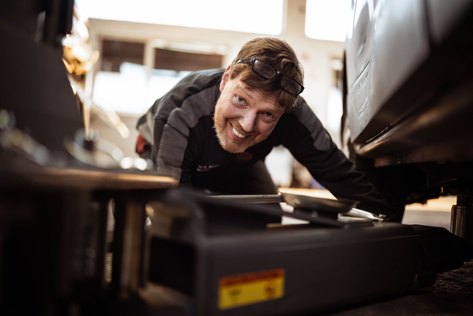 Ein Mann kriecht in einer Garage unter ein Auto und lächelt.