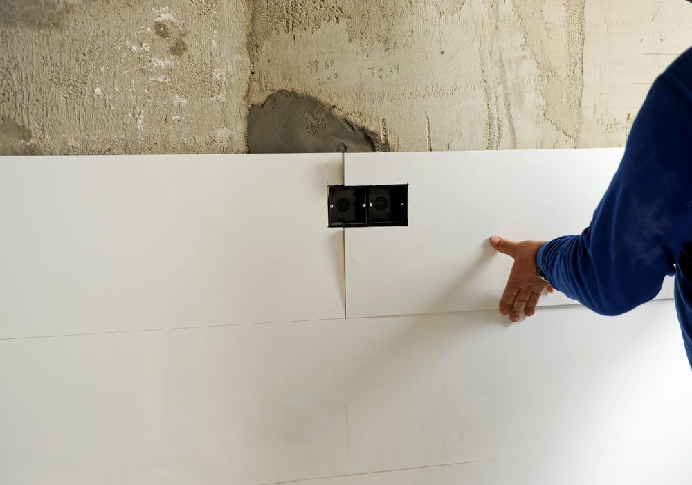 Un hombre sostiene un trozo de azulejo blanco en una pared.