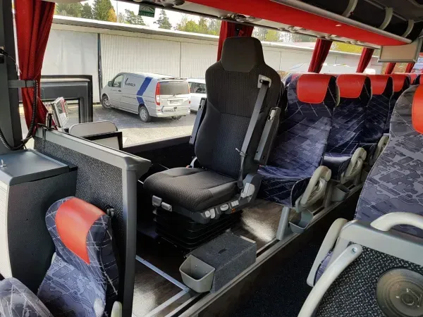 Bussin sisätilat, joissa on rivit punaisia ja sinisiä istuimia sekä yksi musta istuin käytävään päin