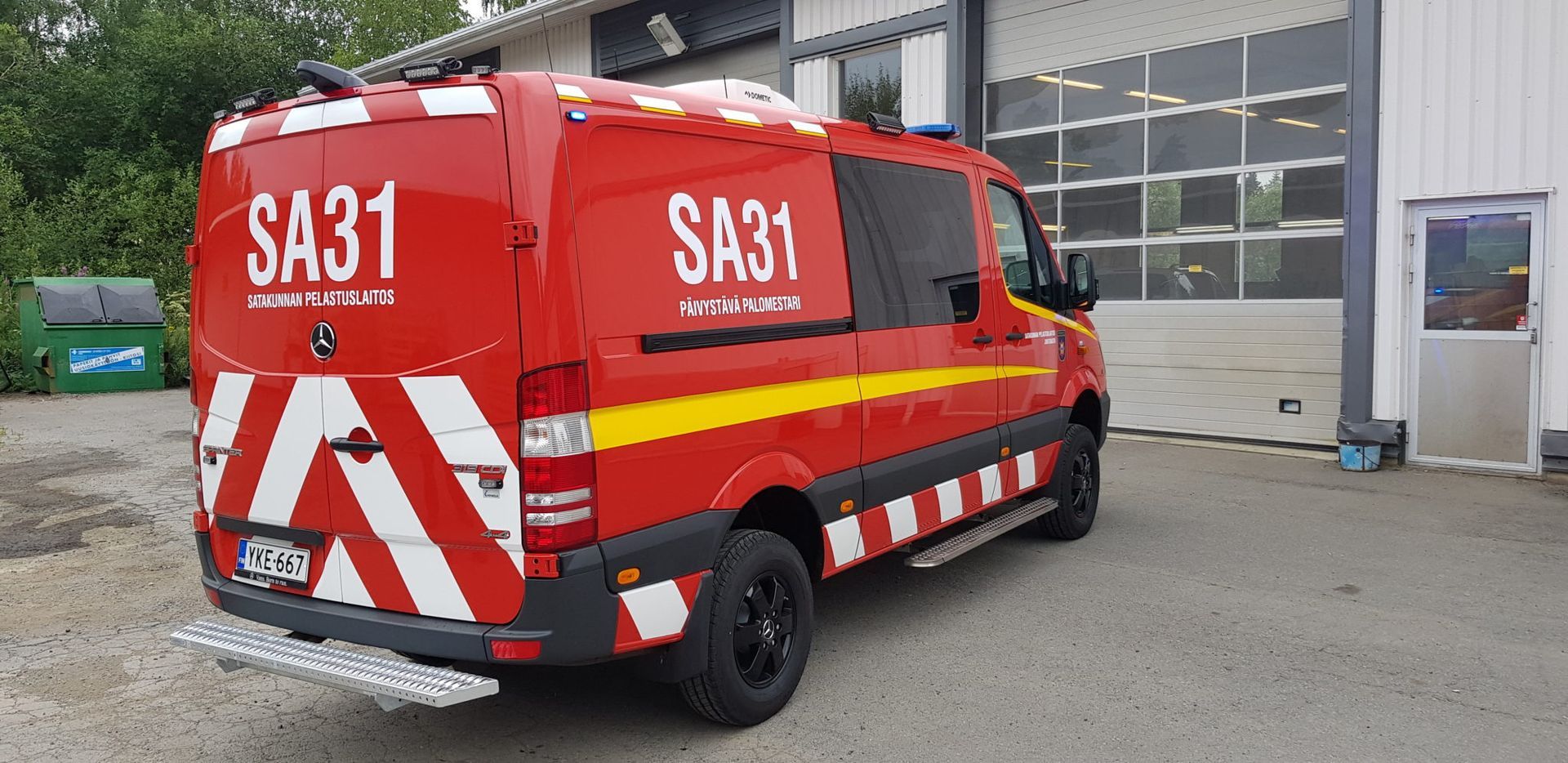 Punainen SA31-merkinnöillä varustettu pelastusauto pysäköitynä rakennuksen viereen
