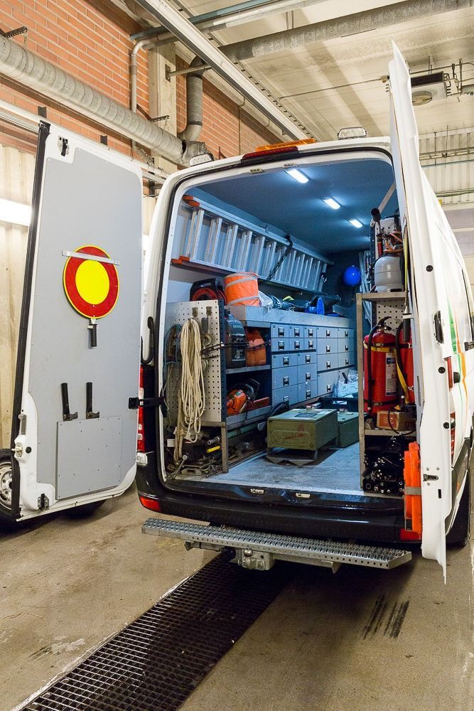 Avoin valkoinen pakettiauto, jossa on sinisellä valaistut laitteet ja säilytyshyllyt autotallissa.