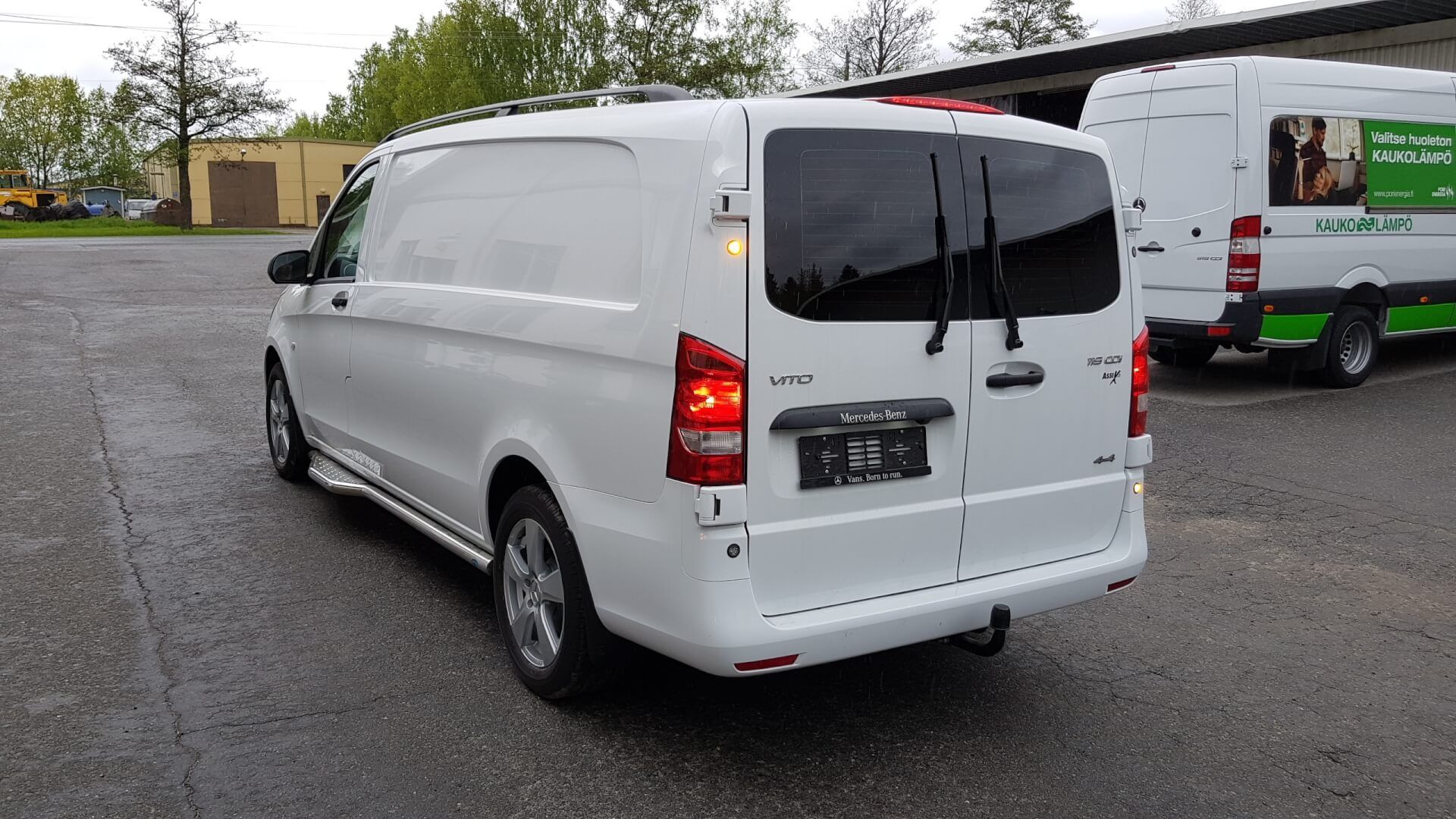 Valkoinen pakettiauto pysäköitynä märälle asfaltille takaovet auki, nähtynä takaa vasemmalta.