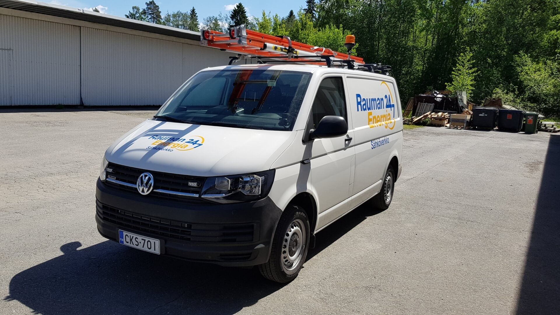 Valkoinen huoltoauto, jonka päällä on punaiset tikkaat, pysäköitynä aurinkoisella teollisuusalueella