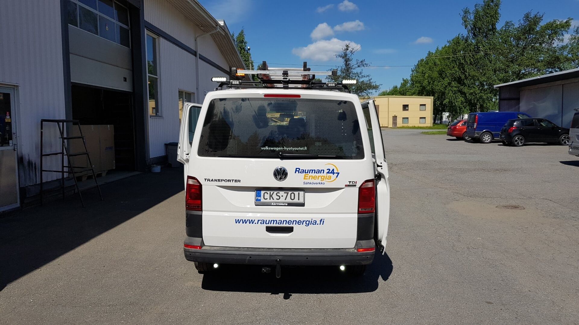 Valkoinen hyötyajoneuvo pysäköitynä teollisuusalueelle rakennuksen viereen kirkkaan sinisen taivaan alle