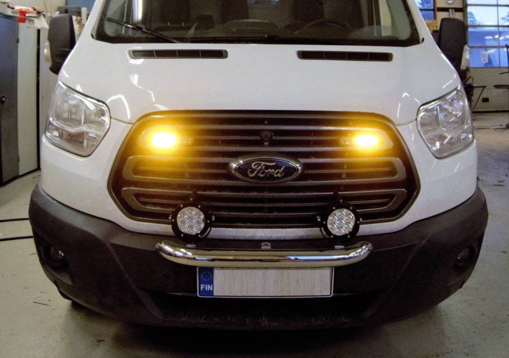 Valkoisen Ford-pakettiauton etukuva, jossa on oranssit valot ja kaksi pyöreää sumuvaloa puskurissa