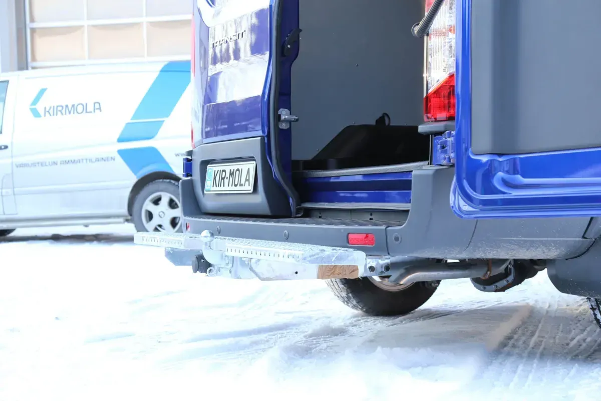Sininen pakettiauto avoimilla takaovilla lumisella kadulla valkoisen kuorma-auton vieressä