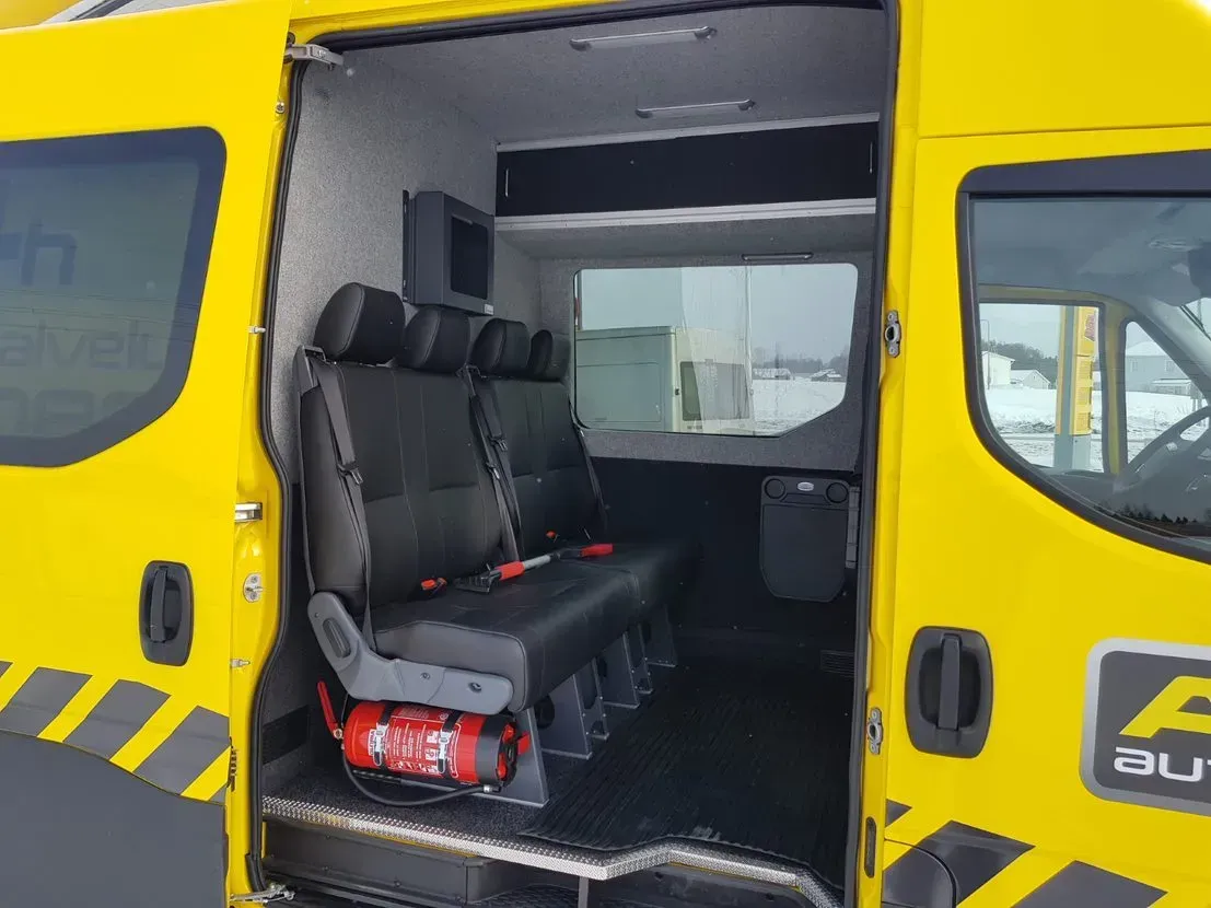 Keltainen pakettiauto, jossa liukuovi auki, mustat istuimet ja punainen sammutin sisällä