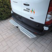 Valkoinen pakettiauto, jonka takapuskurista ulottuu taitettu metallinen askelma päällystetyllä ajotiellä.