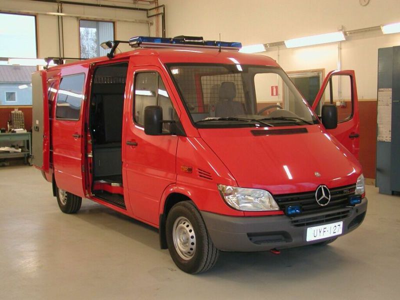 Punainen Mercedes-pakettiauto autotallissa, sivuovi auki ja kattovalot päällä.