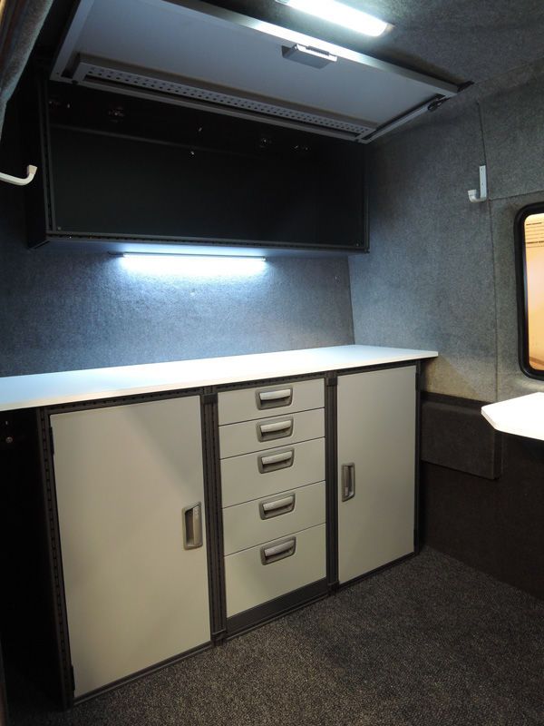 Kompakti toimistokaappien asetelma seinälle kiinnitetyn sermin alla harmaassa sisätilassa.