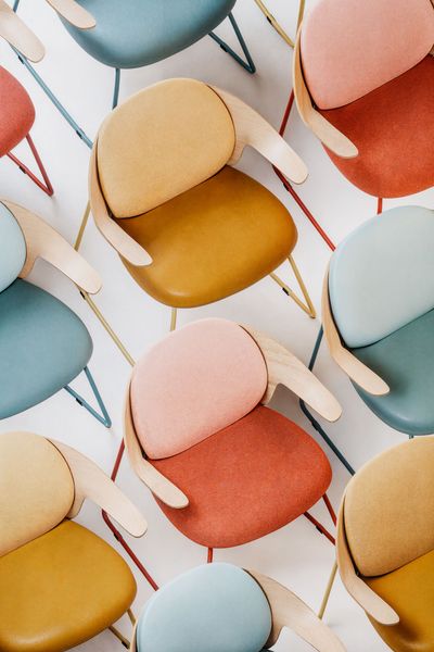 Anordnung moderne Stühle in Gelb, Rosa und Blau mit Holzarmlehnen vor weißem Hintergrund.