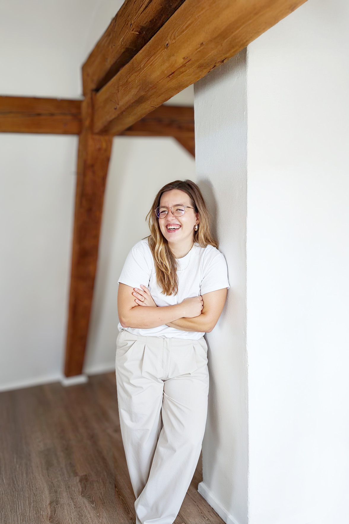 Gründerin Lea Kohlhaas, an eine weiße Wand gelehnt, Arme verschränkt.Holzbalken über dem Kopf.