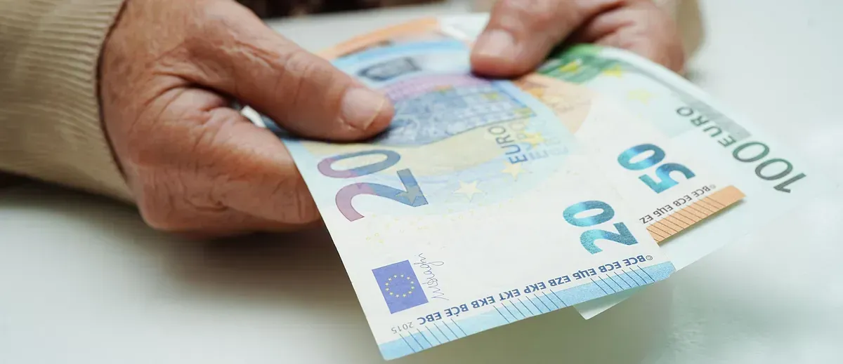 Manos de una persona mayor sosteniendo billetes de euro, incluidos uno de 20, 50 y 100.