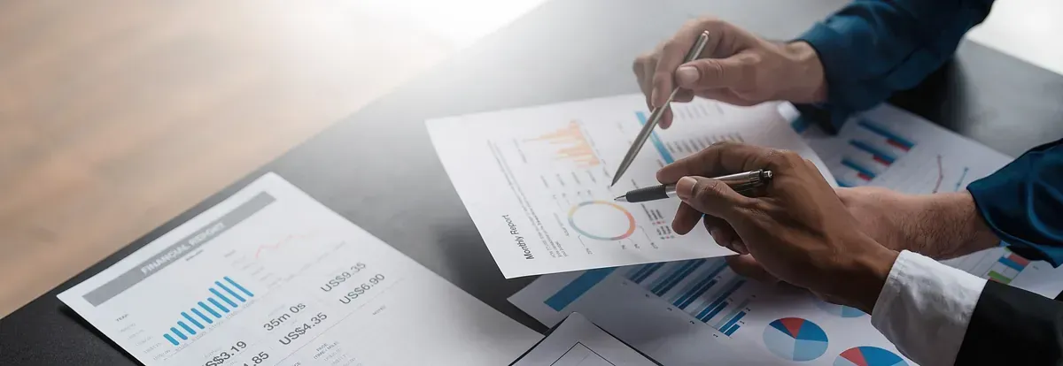 Manos apuntando a gráficos y cuadros en un escritorio durante una reunión de negocios.