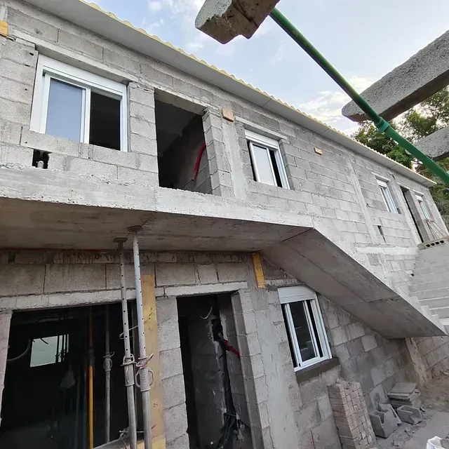 Exterior de una casa de hormigón sin terminar con andamios, ventanas abiertas y una escalera en construcción.