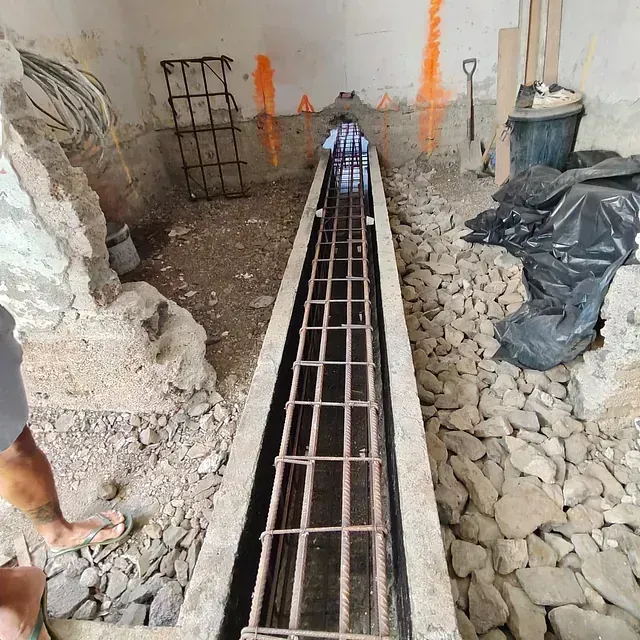 Zanja de construcción con refuerzo de barras de acero y escombros a lo largo de un canal de hormigón estrecho.