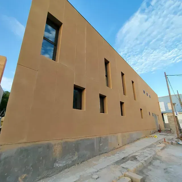 Muro de un edificio de color marrón claro sin terminar con ventanas estrechas a lo largo de un callejón de hormigón.