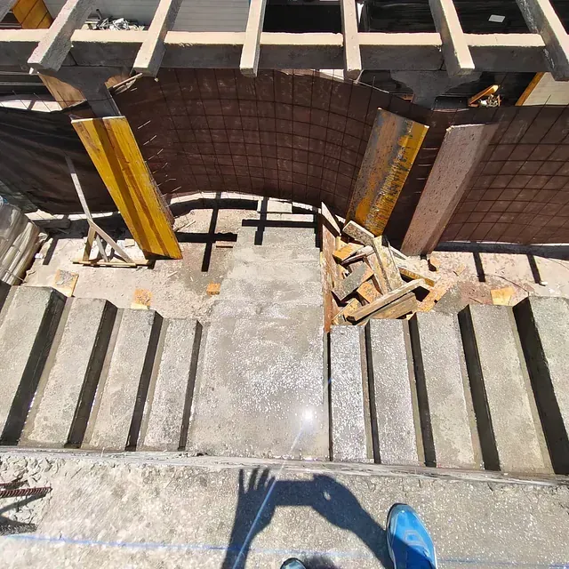 Escalones de hormigón rotos conducen a una puerta oscura, con una sombra y un zapato azul visibles al pie.