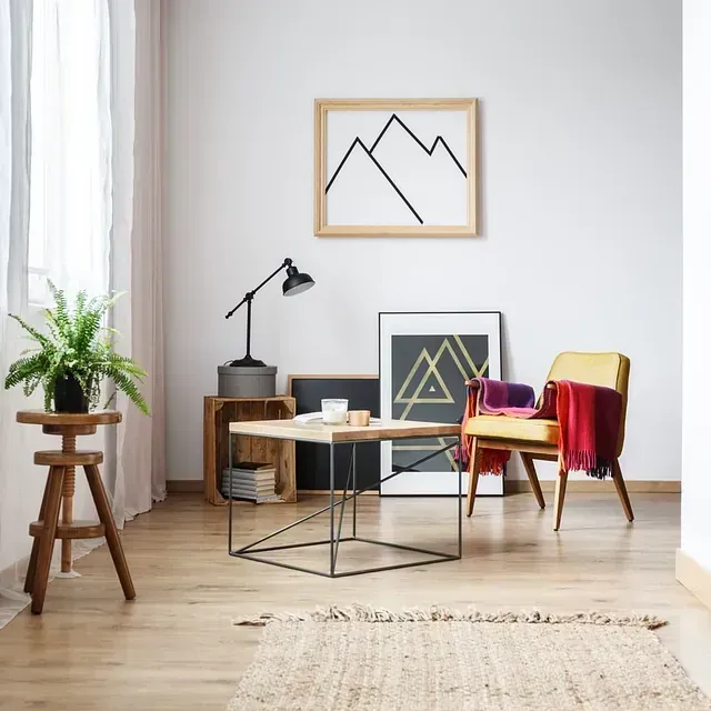 Sala de estar luminosa con sillas modernas, mesa de centro, lámpara, plantas y cuadros minimalistas enmarcados.