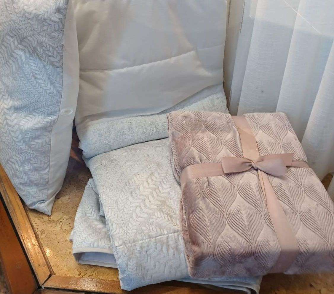 Una pila de mantas y almohadas están sobre una mesa de madera.