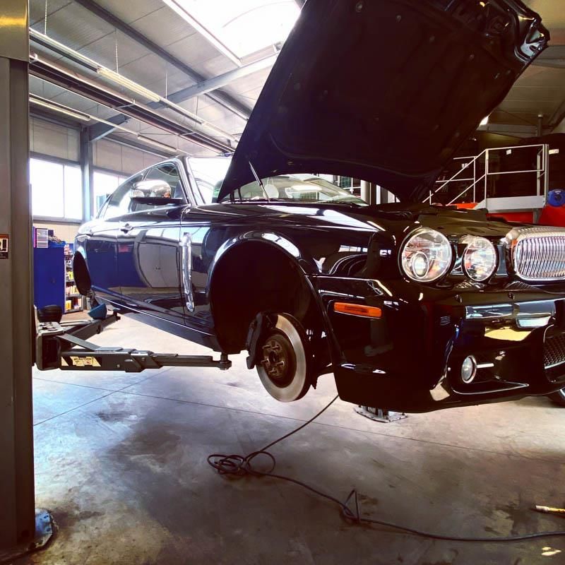 Ein schwarzes Auto mit geöffneter Motorhaube steht auf einer Hebebühne in einer Garage