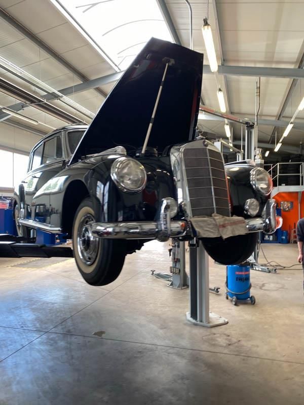 Ein schwarzes Auto mit geöffneter Motorhaube steht auf einer Hebebühne in einer Garage.