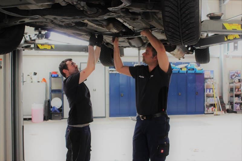 Zwei Männer arbeiten in einer Garage unter einem Auto.