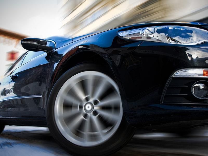 Ein schwarzes Auto fährt eine Straße mit verschwommenem Hintergrund entlang