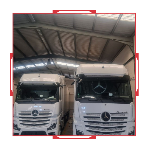 Dos camionetas Mercedes blancas están estacionadas en un almacén.