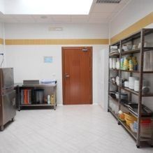 Trastero de cocina comercial con estanterías metálicas, artículos de limpieza y una puerta de madera.